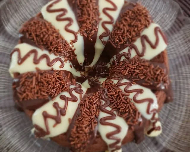 Bolo caseiro coberto de chocolate, com faixas brancas e granulado